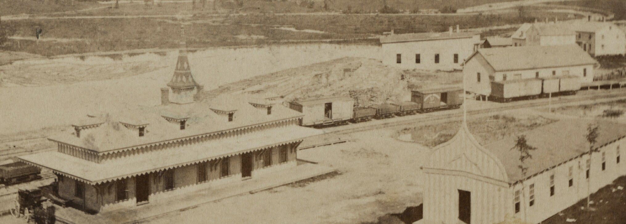 Historic photograph of a railroad station, freight house, and rail yard